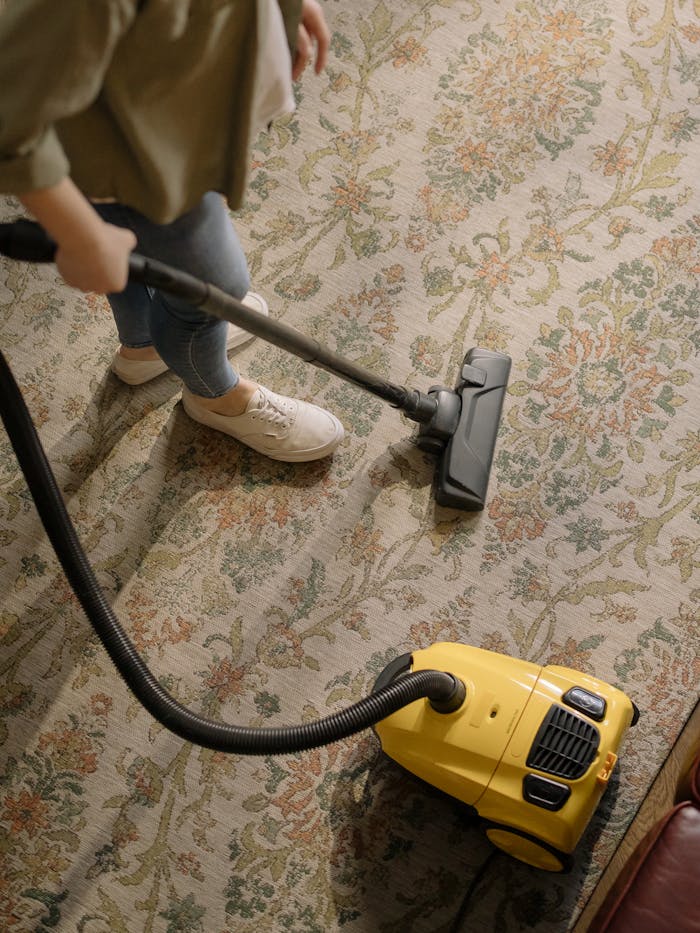who-we-are Person cleaning a floral carpet with a yellow vacuum cleaner indoors.