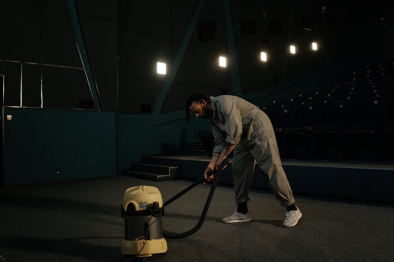 services-02 A cinema employee cleaning the theater floor with a vacuum cleaner under dim lights.