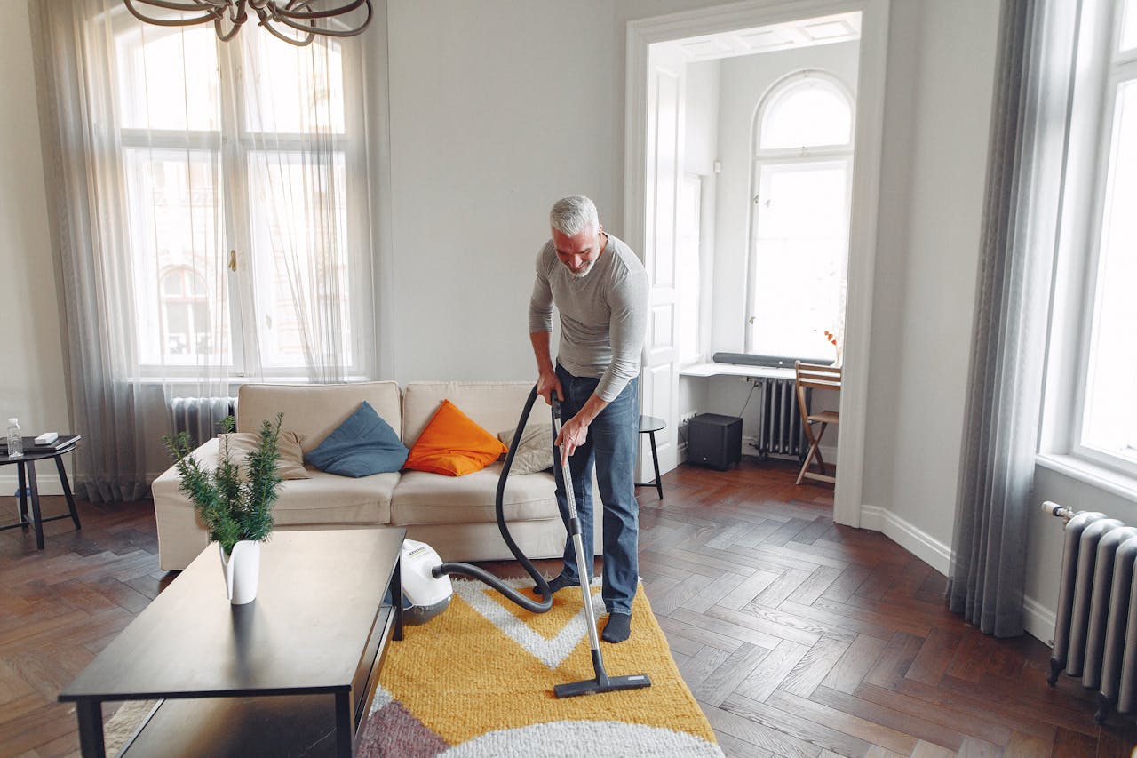 services-04 From above of focused grey haired man with beard vacuum cleaning carpet at home
